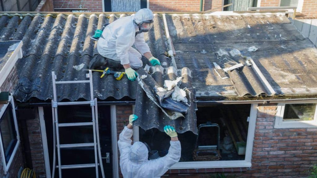 Twee asbestverwijderaars zijn bezig met het vervangen van een asbestdak.