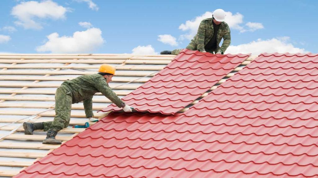 Twee dakwerkers zijn bezig met het toevoegen van nieuwe dakbedekking en het renoveren van het dak.